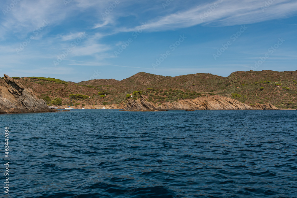 Seaside cliffs, sailboats and houes in Guillola Bay next to Cadaques and Cap Creus, Catalonia, Spain