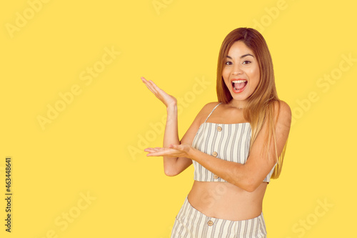 Young latin woman pointing to text, smile and surprise on yellow background.  © Aroa