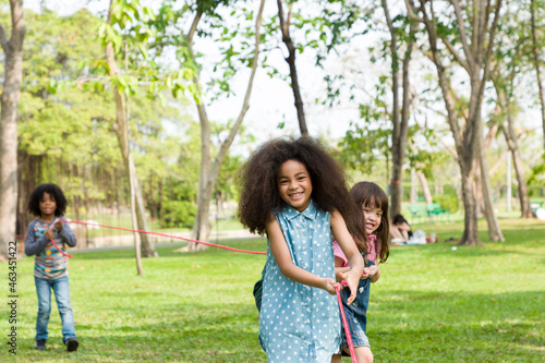 Group of African American boy and girl playing tug of war together in the park. Cheerful diverse children with curly hair having fun with tug of war