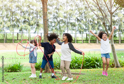 Group of diversity kids playing cheerful in the park. Children having fun and jumping with rope in the garden.