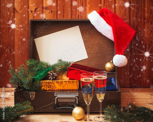 Vintage suitcase with christmas presents, fluffy Santa hat and empty  card for your text. Two glasses of champagne ahead.