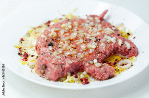 Minced meat with fresh spring onions and spices in the shape of a pig on the white plate, a creatively prepared burger in an interesting shape