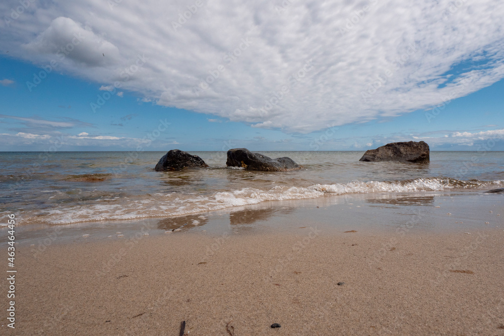 beautiful, smooth sandy beach with some boulders and interesting clouds in blue skies