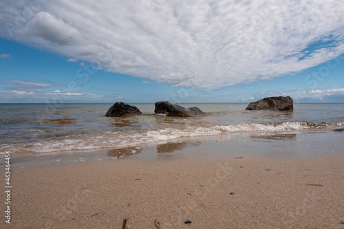 beautiful  smooth sandy beach with some boulders and interesting clouds in blue skies