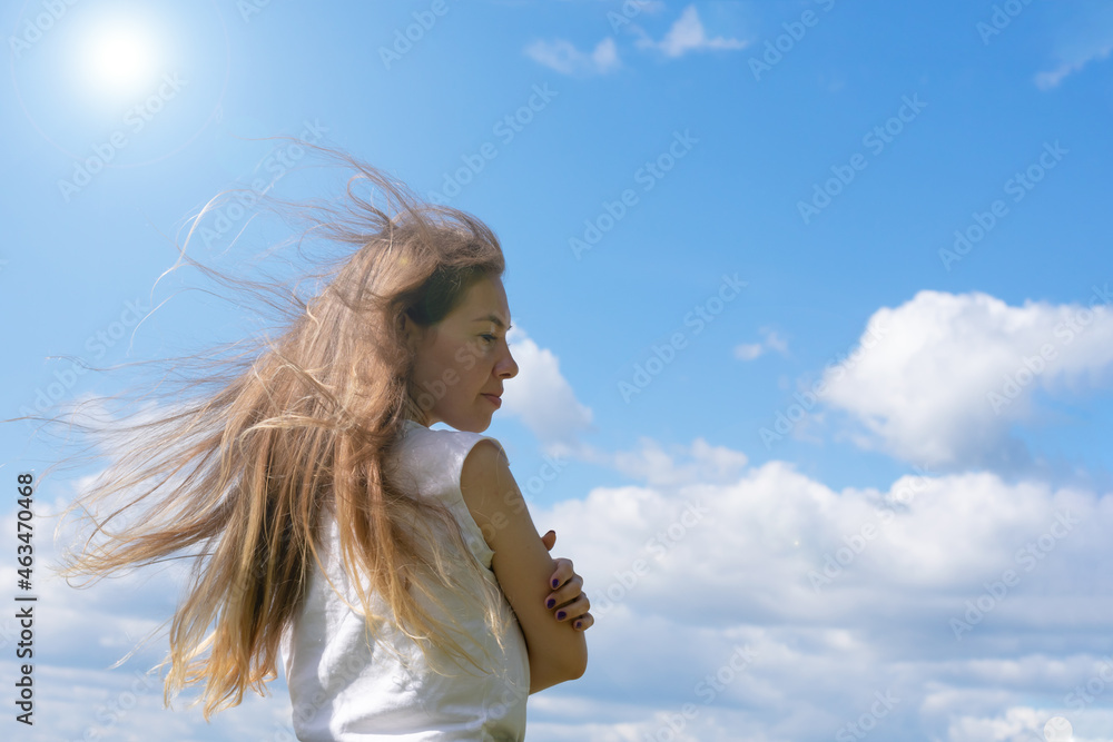 Sunlit young long blond haired woman standing on bright sunlight and blue sky background.Female is hugging and embrtacing herself as concept of calmness harmony and tranquility. Love mood metaphor Sunlit young long blond haired woman standing on bright sunlight and blue sky background.Female is hugging and embrtacing herself as concept of calmness harmony and tranquility. Love mood metaphor
