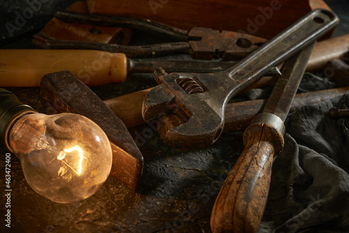 Wooden tool box of used hand tools with old and dirty, rusty wrenches, hammers, and old light bulb