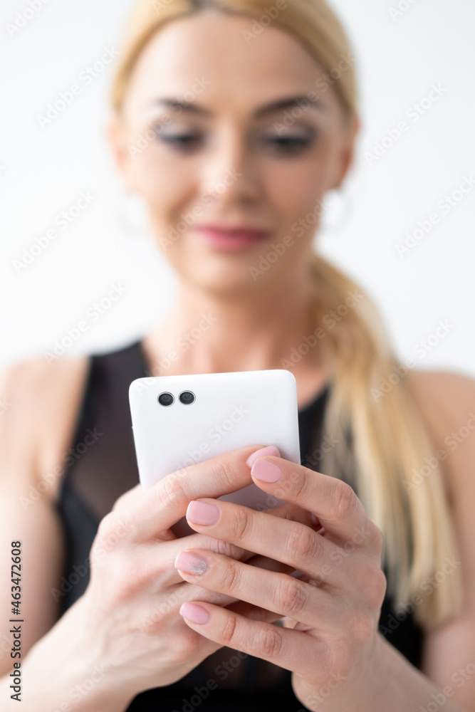 Gadget addiction. Happy woman. Mobile technology. Online lesson. Defocused smiling lady looking on smartphone in hands isolated white. Gadget addiction. Happy woman. Mobile technology. Online lesson. Defocused smiling lady looking on smartphone in hands isolated white.