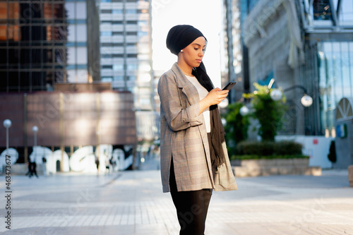 Side view of an adult muslim woman standing in a urban area using her phone