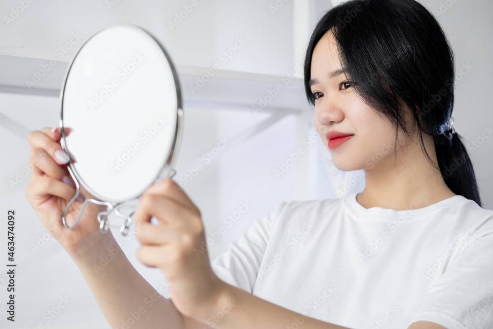 Beautiful asian woman. Perfect skin. Enjoying facial treatment. Pretty smiling lady looking round mirror in light room interior. Beautiful asian woman. Perfect skin. Enjoying facial treatment. Pretty smiling lady looking round mirror in light room interior.