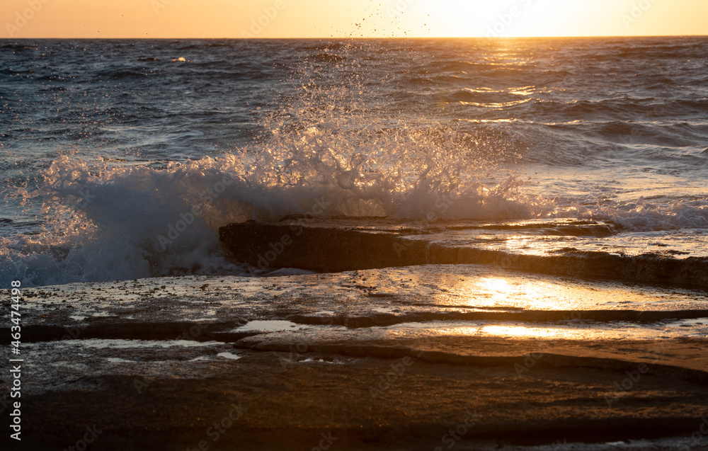Naklejka premium Stormy windy sea waves splashing on a rocky seashore at sunset