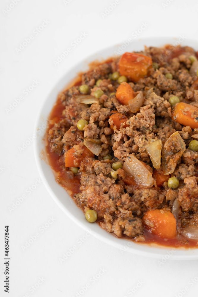 Vegan stew with seitan, carrot, green peas and onion on a white plate. White background, close view. 