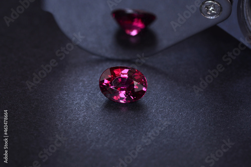 Natural mined oval faceted loose pinkish cherry red unheated rhodolite garnet transparent clean setting for jewelry making. Black pattern radial gradient dark background. Reflection on metal surface.