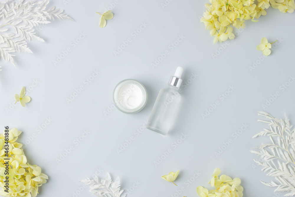 Cosmetic skin care products with flowers on grey background. Flat lay.