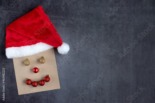 The face of a smiling Santa Claus is made of craft paper, the brightening balls and a Christmas cap. Creative ideas, dark background, place for design and text. Concept creativity, Christmas.