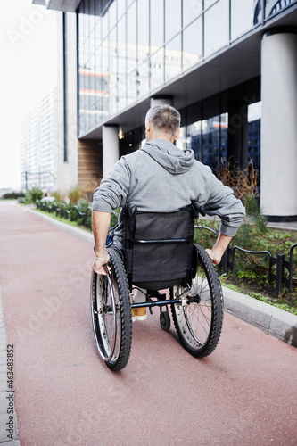 Rear view of mature male patient riding in wheelchair along the street outdoors
