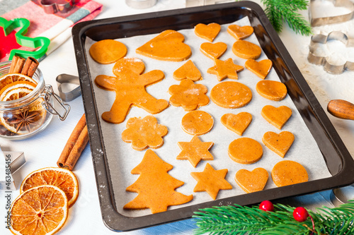 Raw gingerbread cookies on a baking sheet, metal cutter, Christmas spices and decoration on table