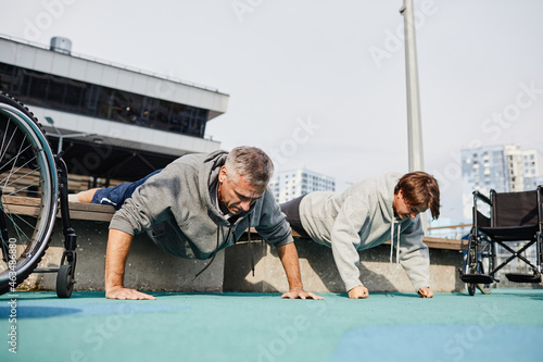 Mature couple with disability training together outdoors, they doing push-ups to train their hands