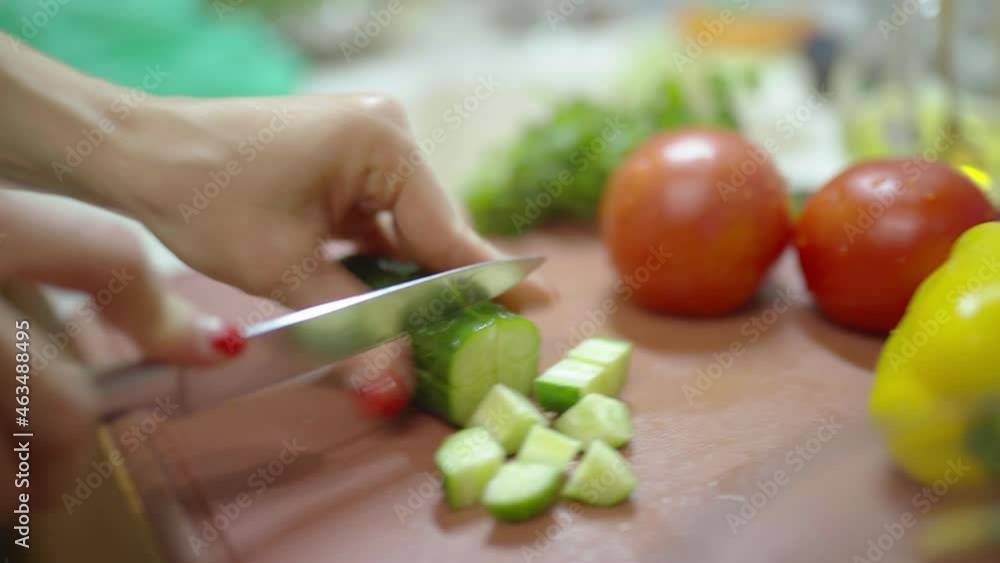 healthy eating, vegetarian food and cooking concept - young woman with kitchen knife chopping cucumber on wooden cutting board at home