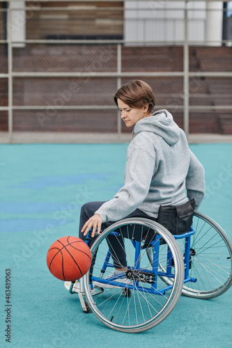 Mature paraplegic woman sitting in wheelchair playing basketball on sport ground