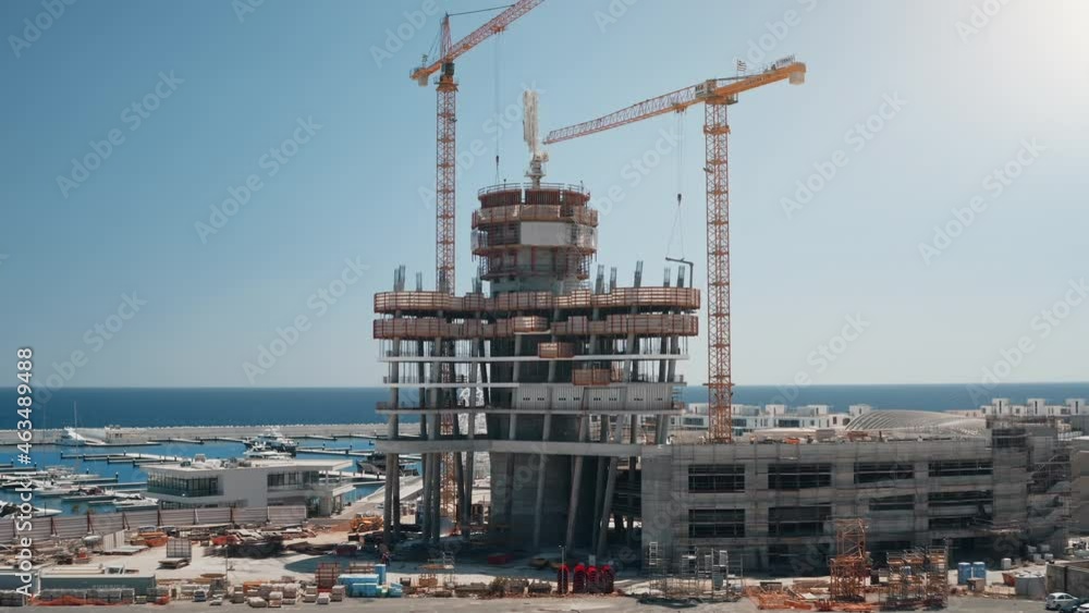 High cranes works on new building construction. Architechture landscape on sea coast. Infrastructure and development. Real estate project construction site with high tower. Aerial drone flight High cranes works on new building construction. Architechture landscape on sea coast. Infrastructure and development. Real estate project construction site with high tower. Aerial drone flight