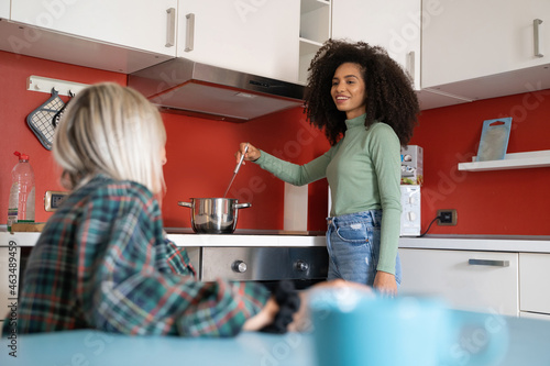 Canvas Print Two young multiracial students girls cooking in the youth hostel kitchen talking