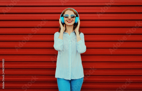 Portrait of happy smiling young woman with headphones listening to music on a colorful red background