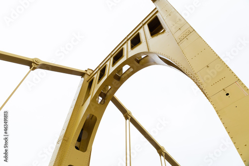 Bright yellow painted upright metal truss of a self anchored suspension bridge against an overcast sky, horizontal aspect photo