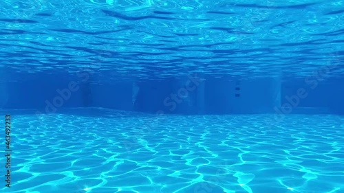 The view through a viewing port between floor, bottom and surface of swimming pool blue water with sun reflections and water ripples, at the resort 