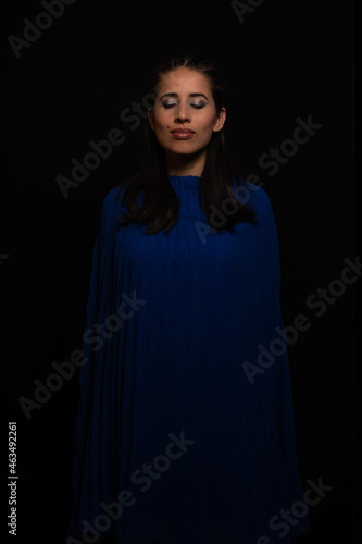 Latin woman. model, young with light skin, tanned. model. with continuous light, shadows and ring of light. Model with eye makeup. green eyes. on black background. dressed in blue. portrait, model.