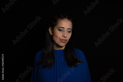 Latin woman. model, young with light skin, tanned. model. with continuous light, shadows and ring of light. Model with eye makeup. green eyes. on black background. dressed in blue. portrait, model.