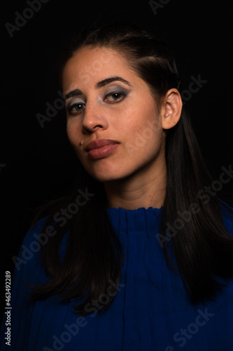 Latin woman. model, young with light skin, tanned. model. with continuous light, shadows and ring of light. Model with eye makeup. green eyes. on black background. dressed in blue. portrait, model.