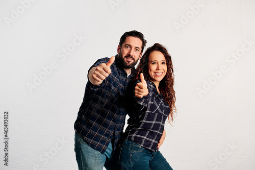 An adult couple in plaid shirts showing thumbs up to the camera and smiling against a white background