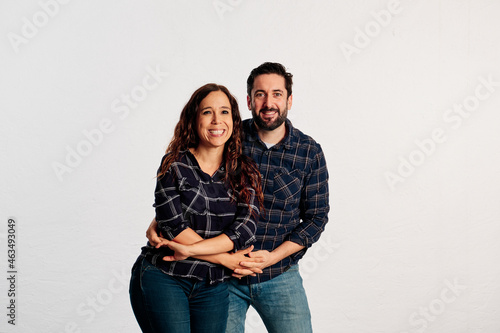 An adult couple in plaid shirts showing thumbs up to the camera and smiling against a white background