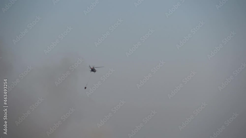 Helicopter flies with cargo. Bambi bucket from below on rope.