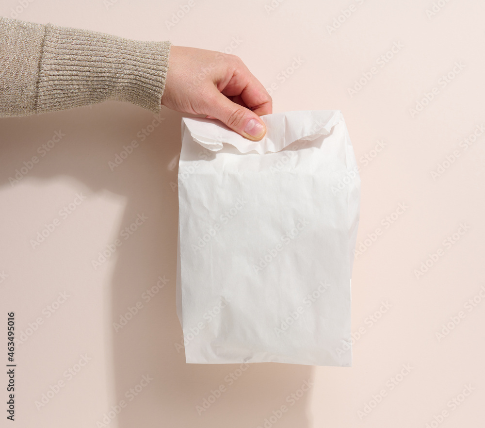 female hand holds a full paper bag on a beige background. Refusal from plastic packaging, food delivery female hand holds a full paper bag on a beige background. Refusal from plastic packaging, food delivery