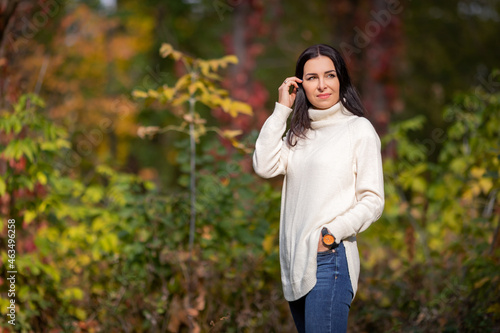 A young girl stands straightening her hair in an autumn park in a white sweater and blue jeans. High quality photo