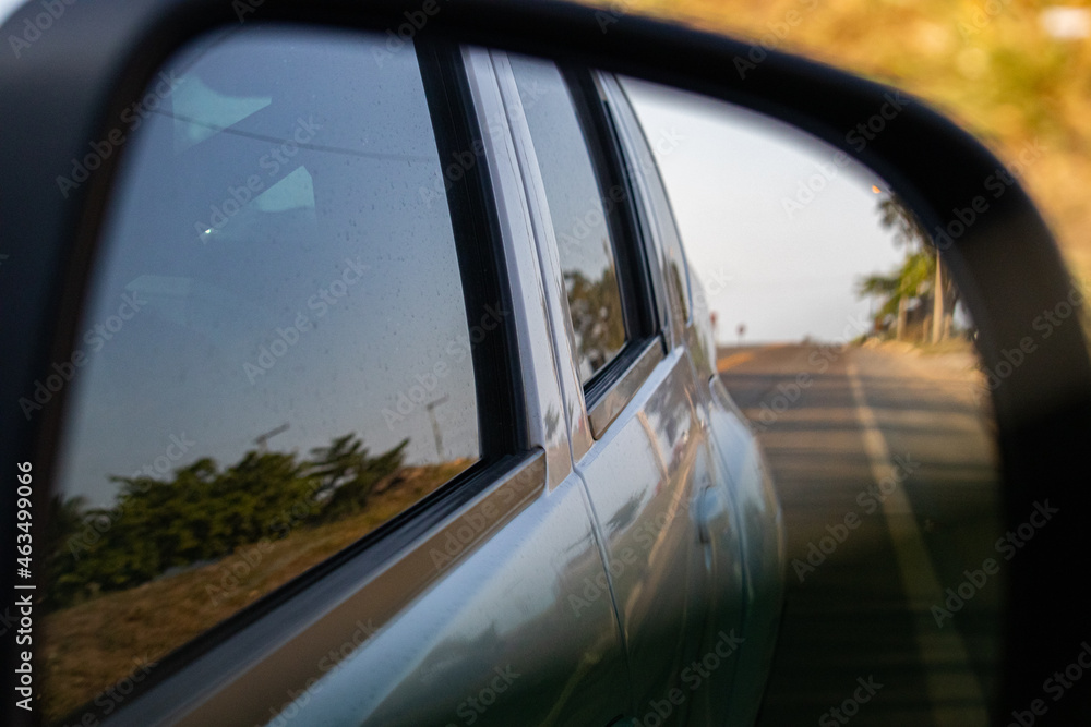 reflection of the road and trees in a car's rearview mirror