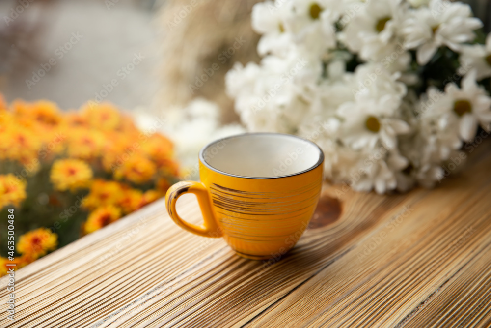 Yellow cup on a wooden surface on a blurred background with flowers.