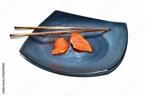 Fresh raw salmon, sliced, sliced ​​with chopsticks in a black plate on a white background.