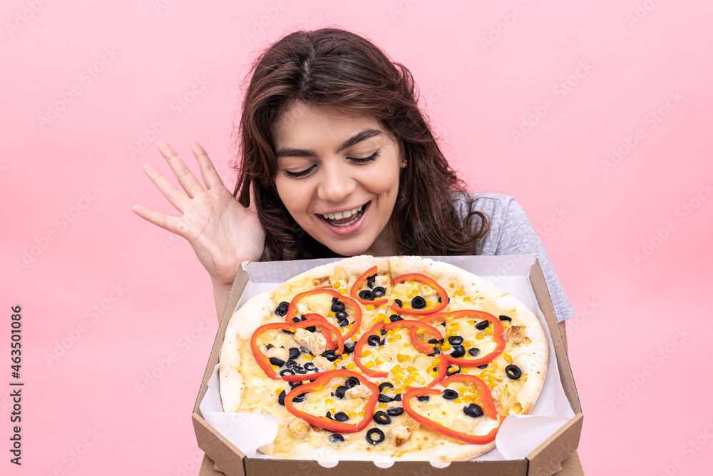 Attractive girl with pizza in a box for delivery on a pink background.