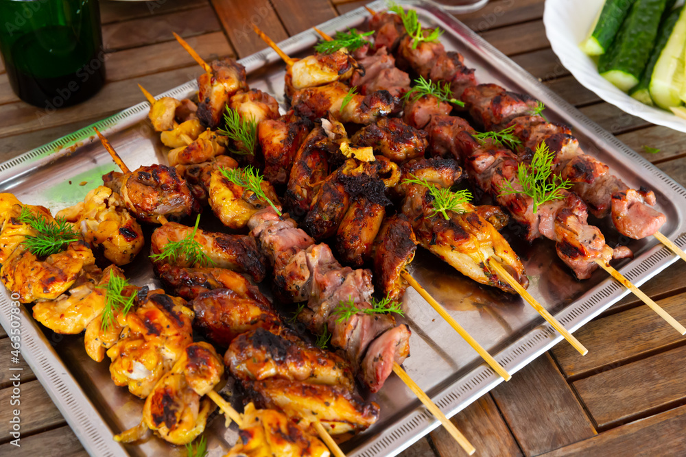 Appetizing shashliks of pork meat and chicken grilled on skewers served with fresh cucumbers and greens