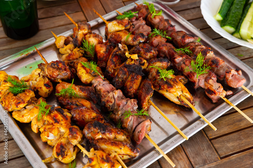 Appetizing shashliks of pork meat and chicken grilled on skewers served with fresh cucumbers and greens