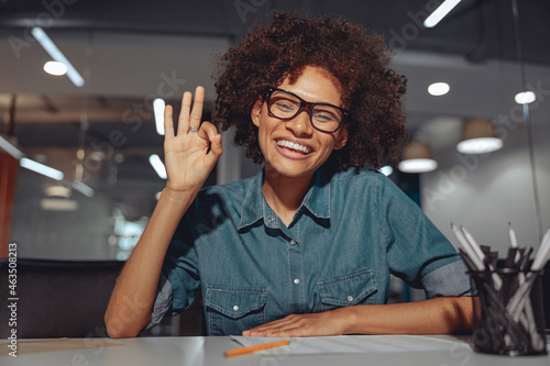 Smiling Afro American lady in glasses communicating in sign language while looking at camera photo