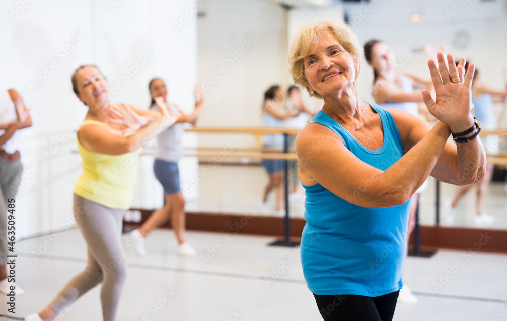 Portrait of an active mature European woman enjoying modern energetic dancing in a female group in the studio
