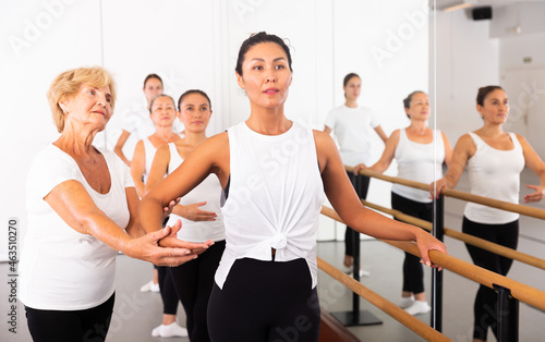 Women of different ages standing in row and training ballet moves. Their senior trainer correcting them.