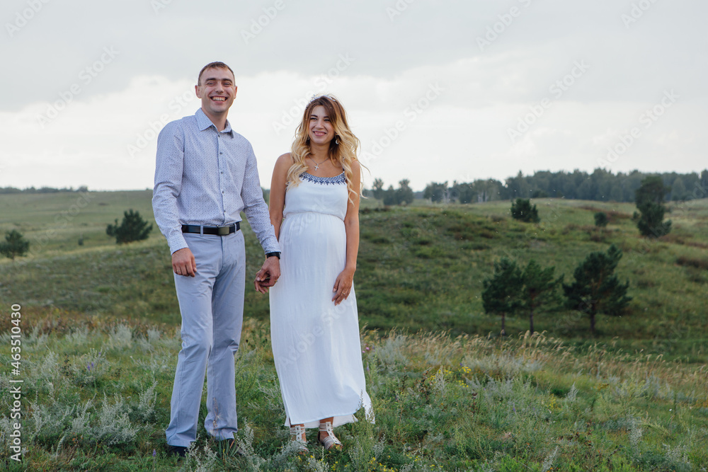 Happy young couple, expecting a baby. Man hugs his pretty pregnant woman in a white dress outdoors. Happy young couple, expecting a baby. Man hugs his pretty pregnant woman in a white dress outdoors.