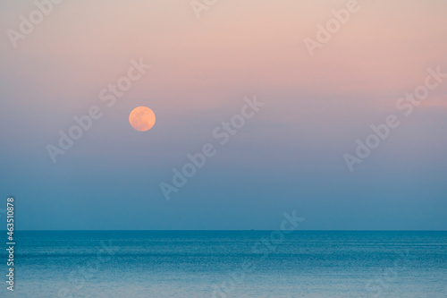 Full moon over the sea against the background of the colorful sky