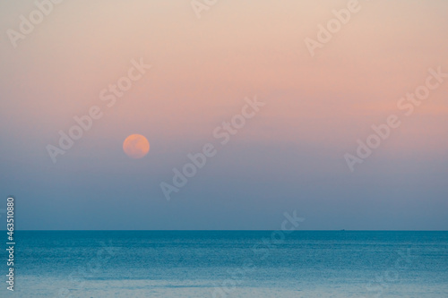 Full moon over the sea against the background of the colorful sky