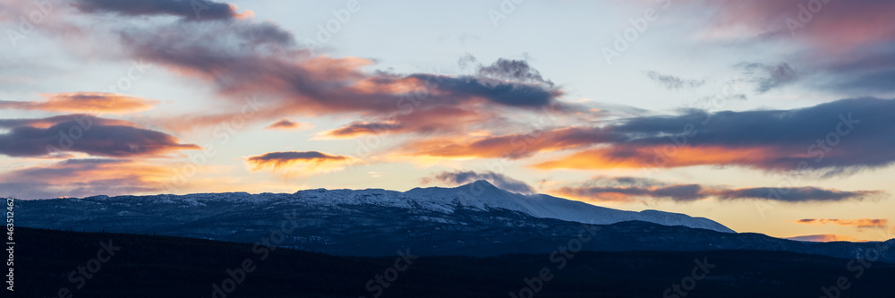 Sunset over boreal forest in northern Canada with dark theme. Snow capped mountains, pink, pastel sky. 