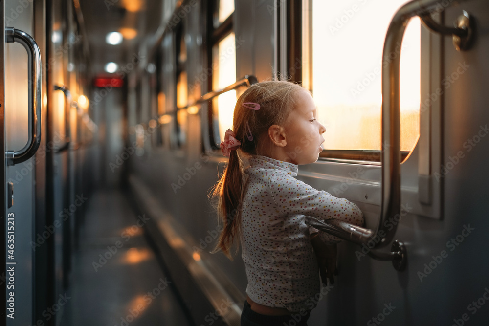 Obraz premium Toddler child looking though train window on sunset, bright sunlight, atmospheric travel by railway with kids. Girl happy exploring the way in evening. Exciting family trip
